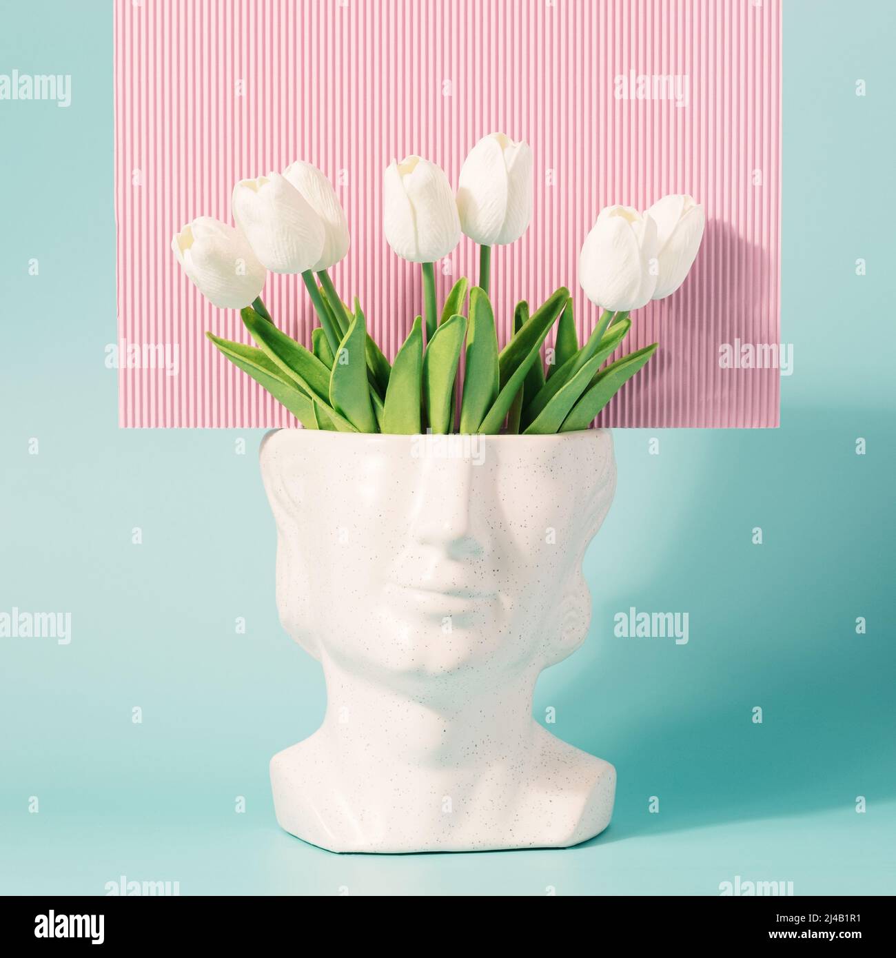 Retro head sculpture with tulip flowers on a pastel blue pink background. Spring, summer retro wave concept. Stock Photo