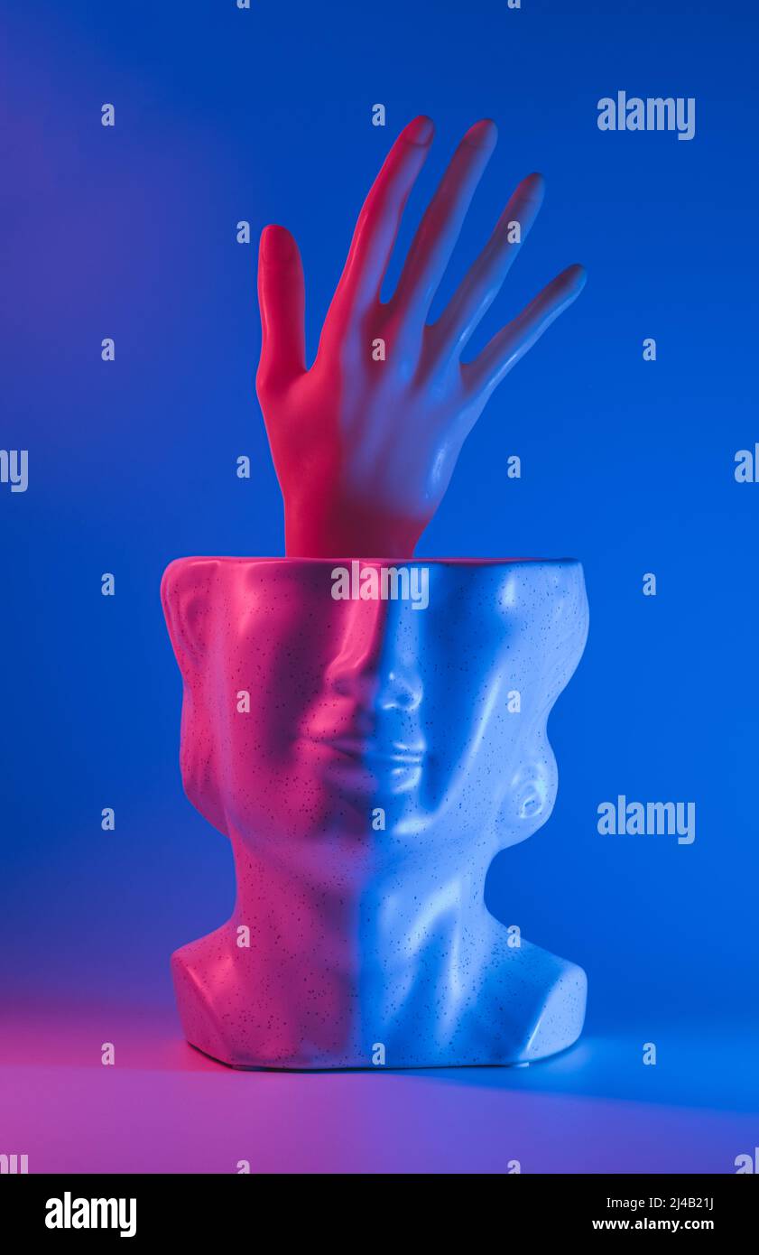 Hand reaching out from statue head and pink blue led lights. Neon, help surreal background. Stock Photo