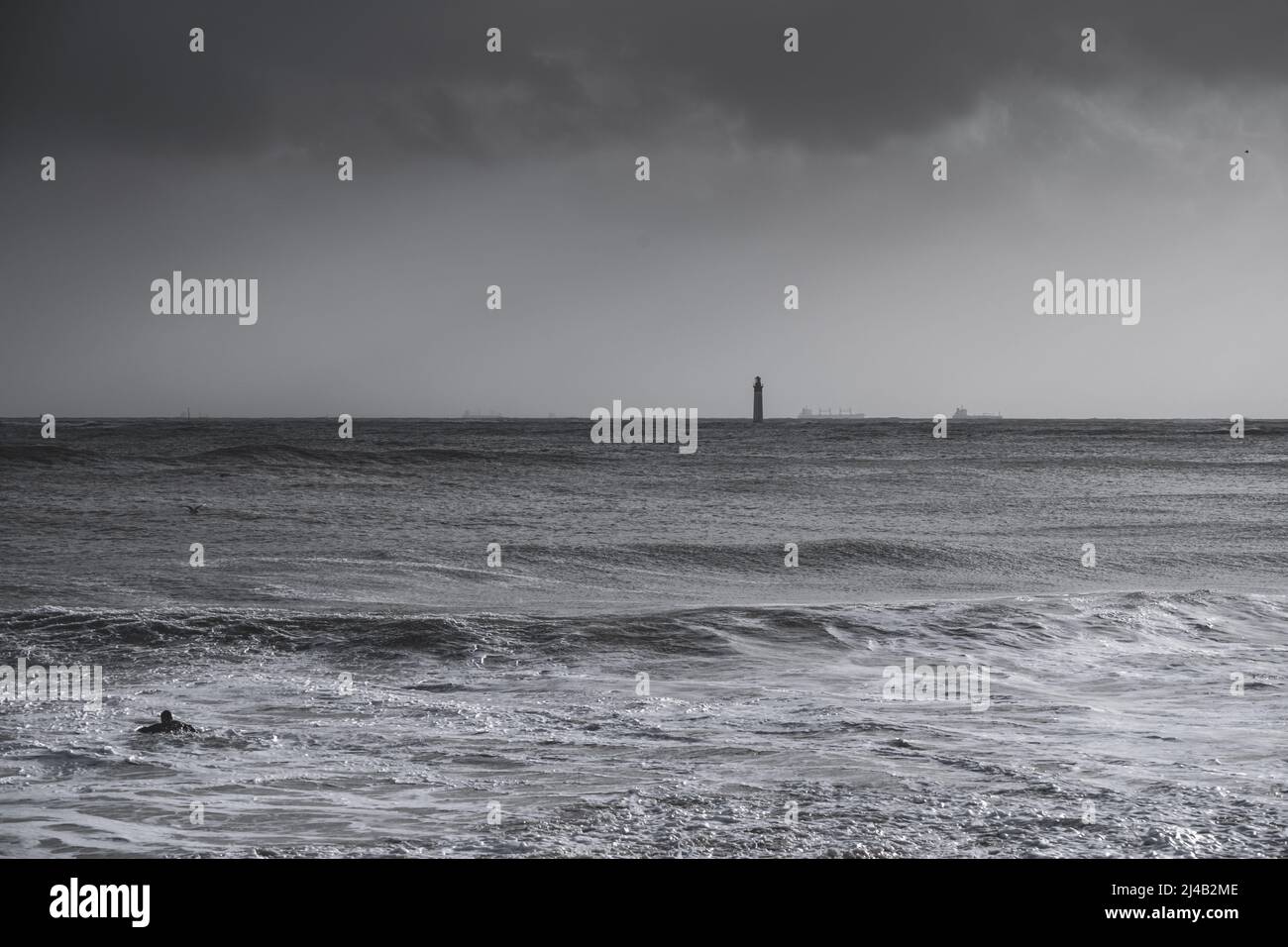 silhouette of surfer in waves with Chauveau lighthouse, the famous lighthouse near La Rochelle and Re island Stock Photo