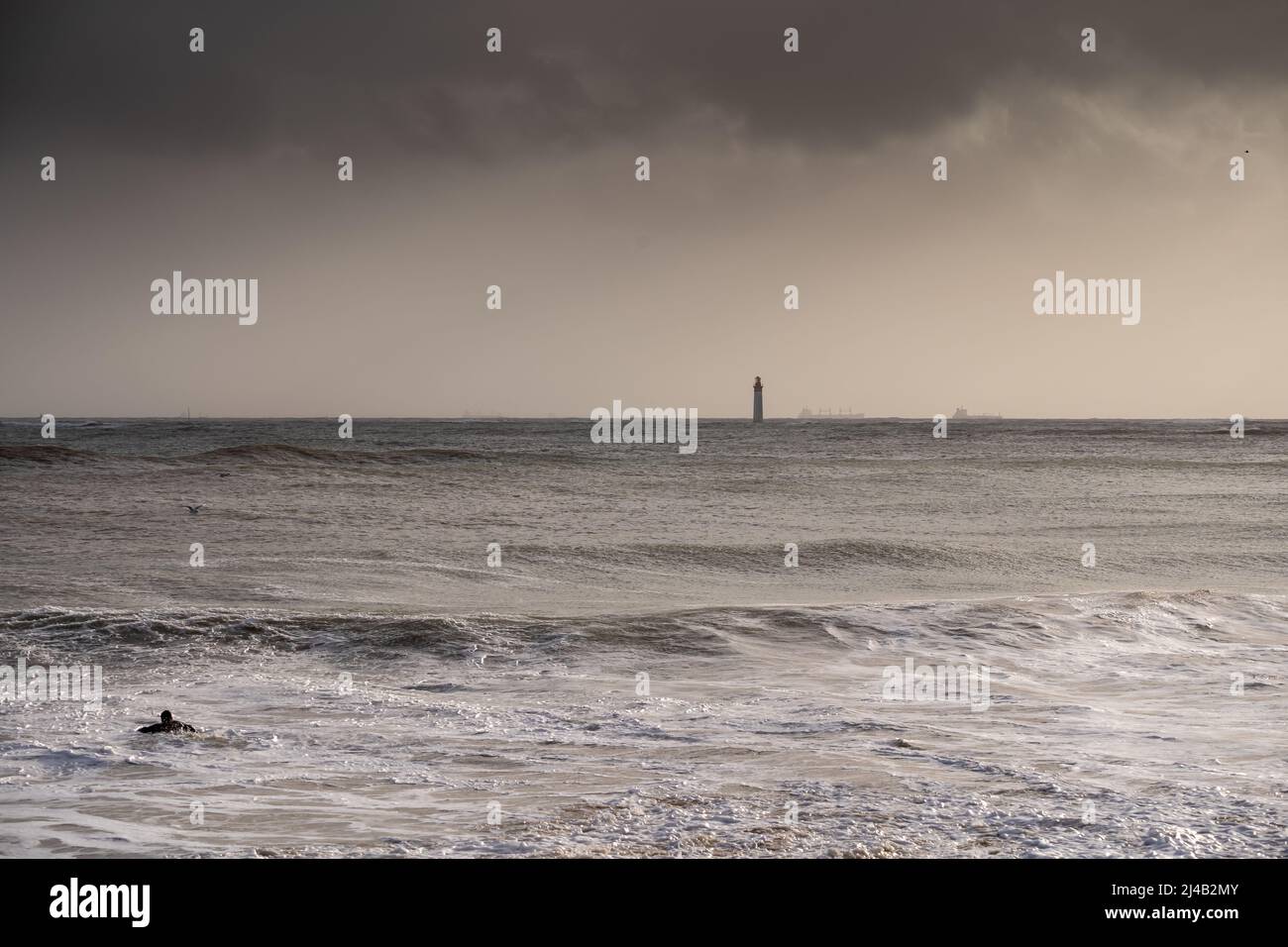 silhouette of surfer in waves with Chauveau lighthouse, the famous lighthouse near La Rochelle and Re island Stock Photo