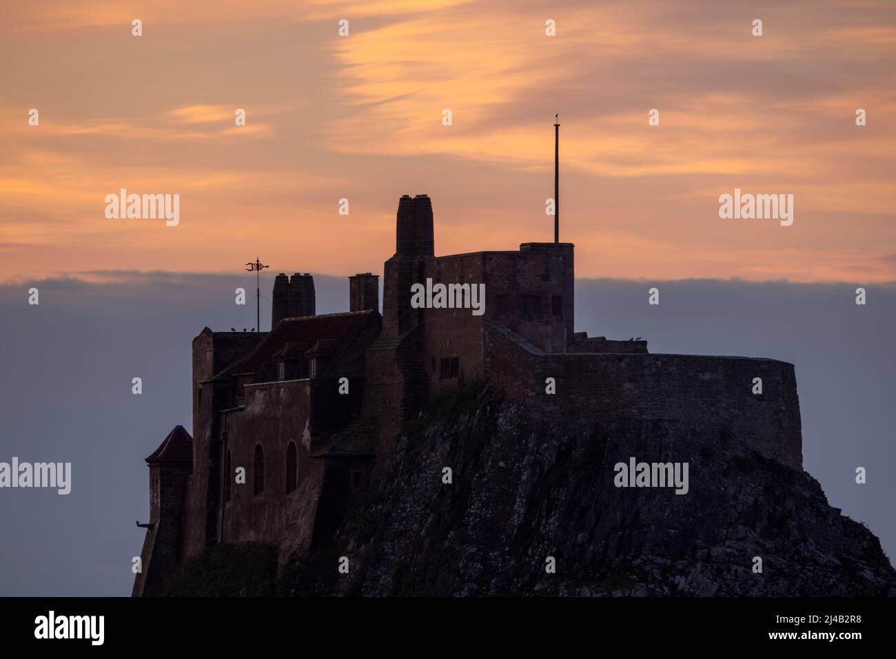 Holy Island castle moments before the sun rises into a red & yellow sky Stock Photo