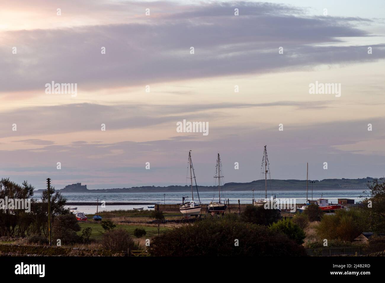 'Beached' sailing boats with birds perched in their rigging and Bamburgh Castle on the horizon at dawn Stock Photo