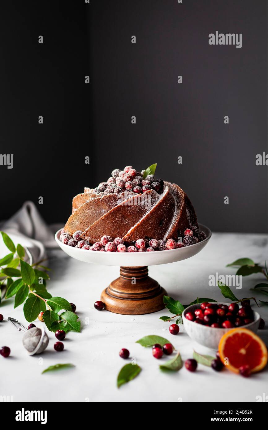 Cranberry orange bundt cake on a marble surface with cranberry leaves and oranges Stock Photo
