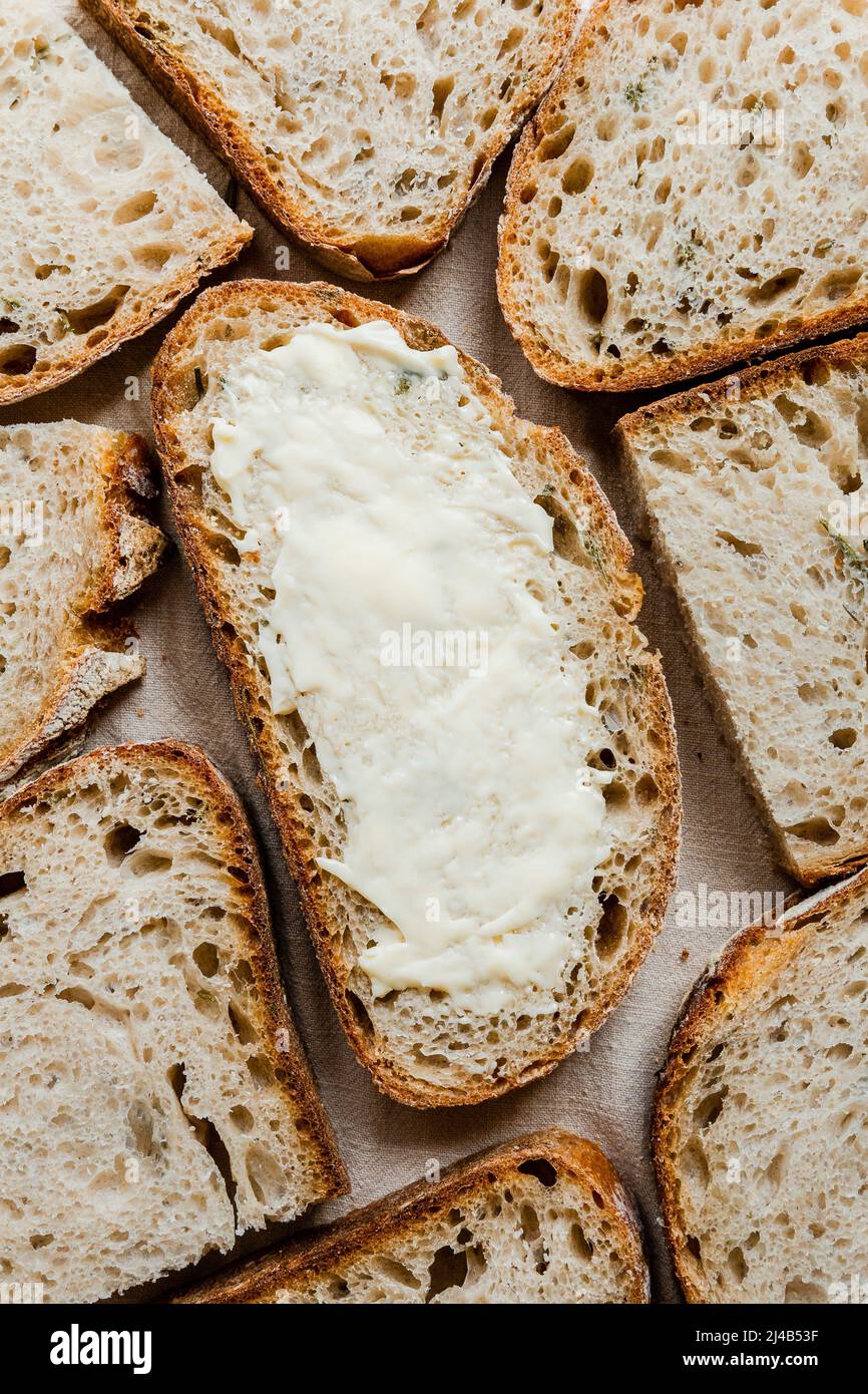 Buttered slice of rosemary sourdough bread, surrounded by many slices. Stock Photo