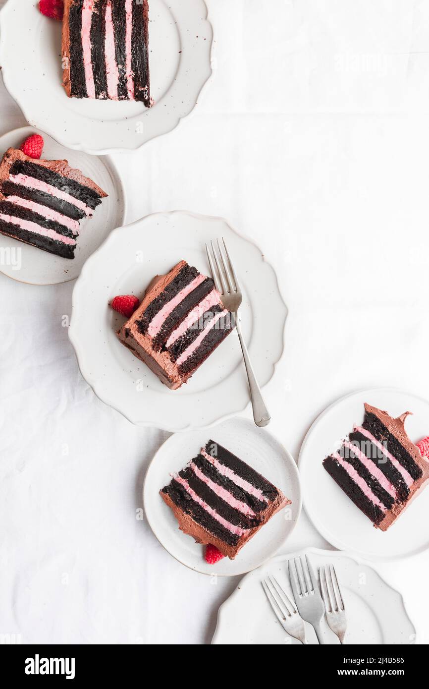 Multiple slices of raspberry and chocolate cake, on plates with forks. Stock Photo