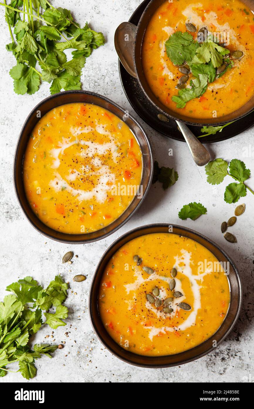 Three bowls of carrot soup with various garnishes including coconut milk, pumpkin seeds and fresh ciriander. Stock Photo