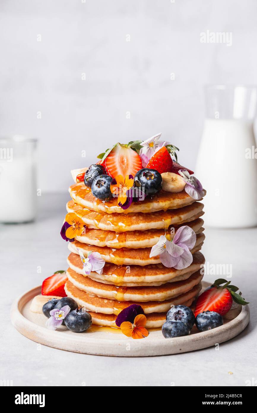 Pancakes, served with strawberries, blueberries, banana, edible flowers and syrup. Stock Photo