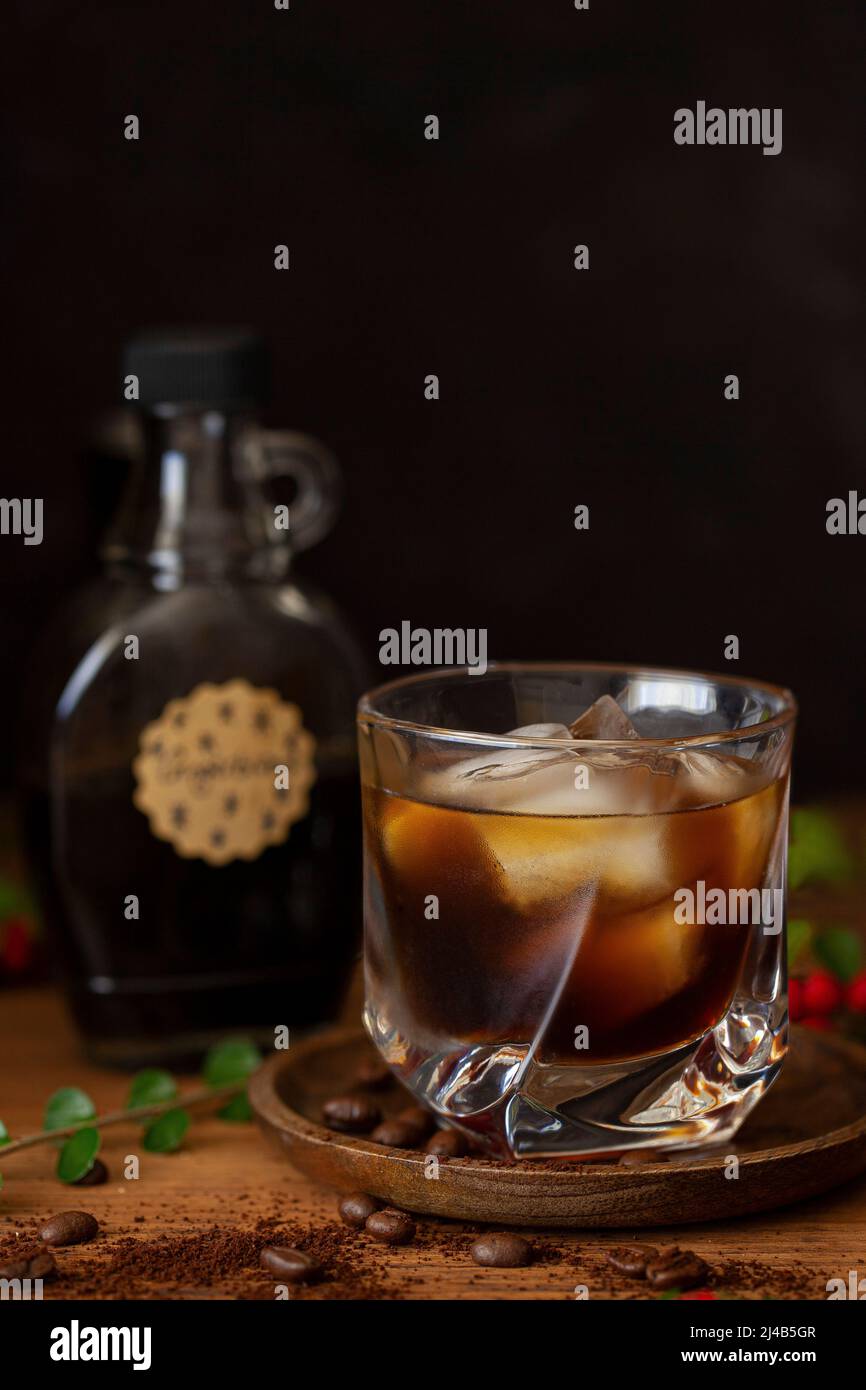 A black Russian cocktail flavoured with gingerbread syrup and a bottle of gingerbread syrup is out of focus behind the glass. Stock Photo