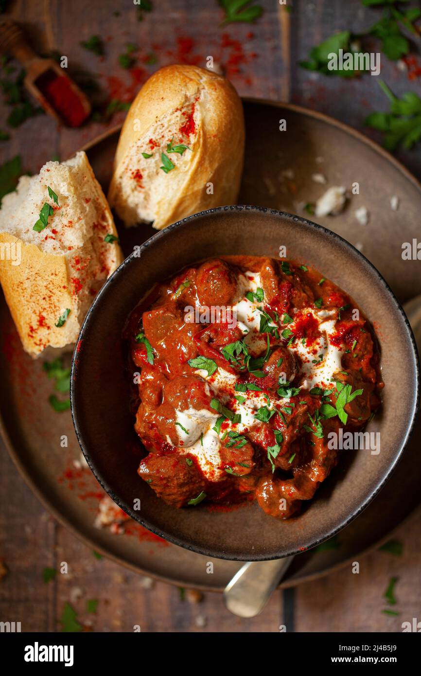 A bowl of beef goulash topped with soured cream and parsley with a side of cursty bread. Stock Photo