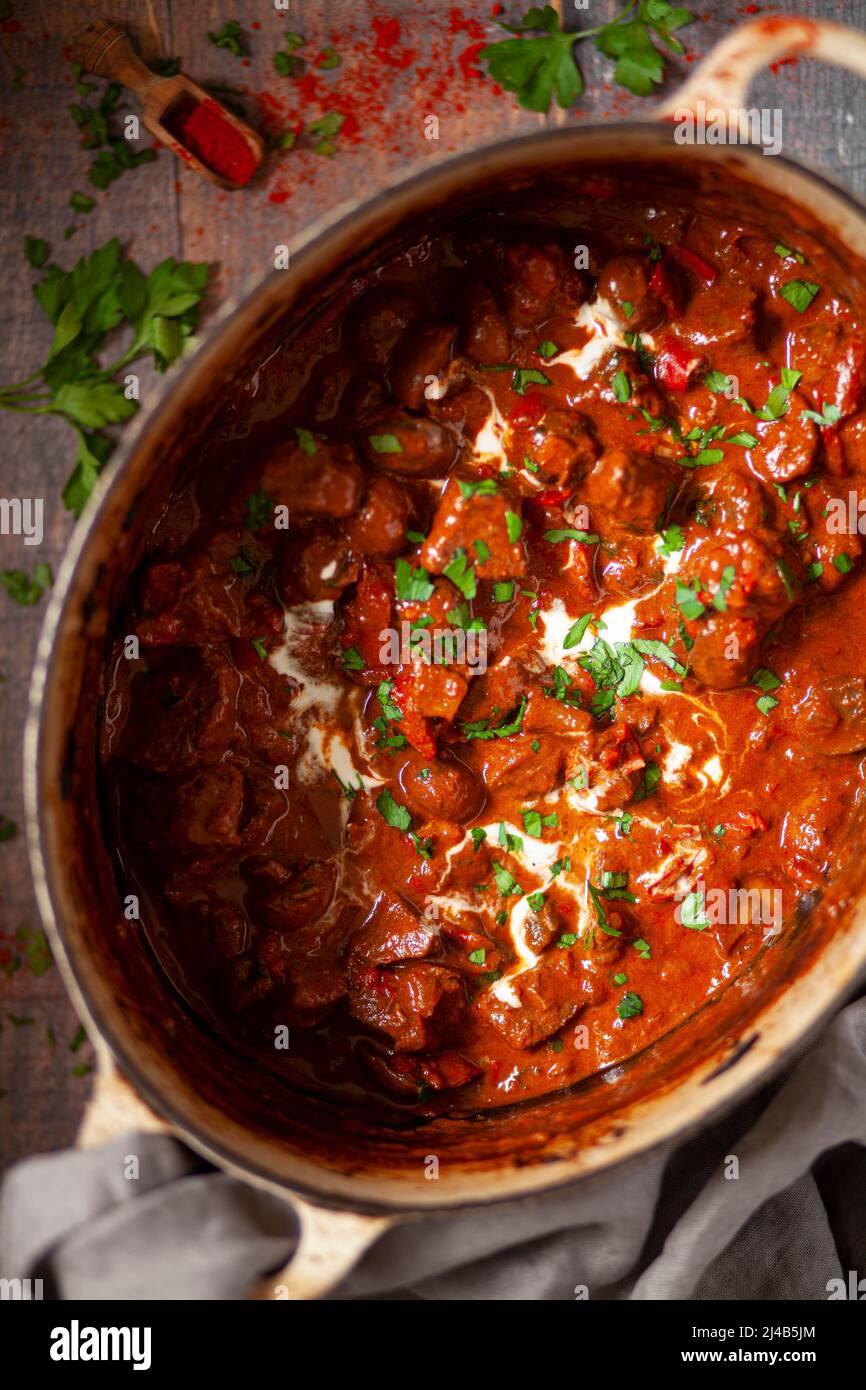 Slow cooked beef goulash in a Dutch oven garnished with soured cream and parsley. Stock Photo