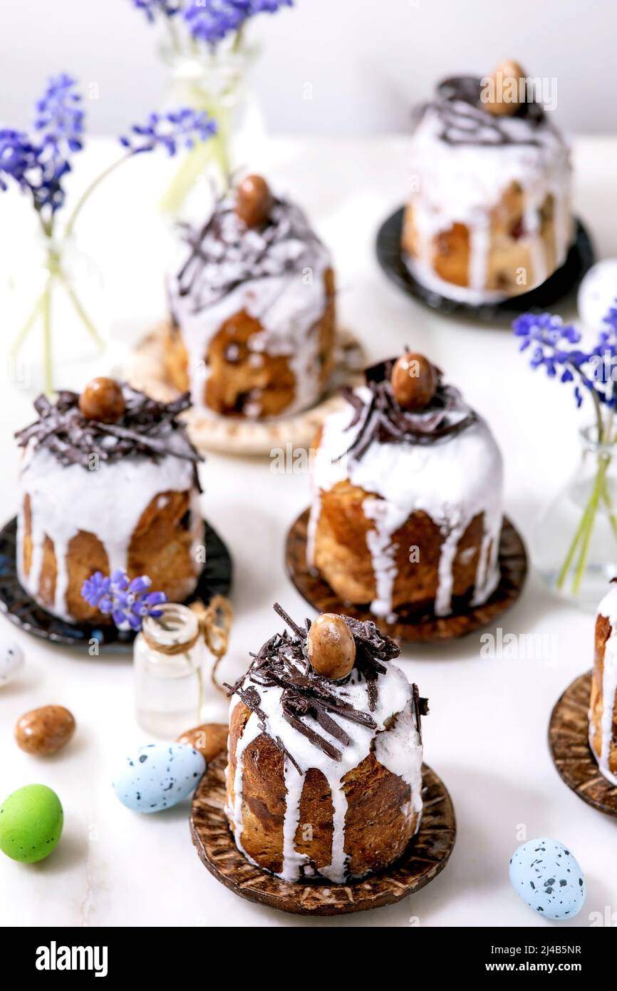 Homemade traditionla small Easter kulich cakes with chocolate nests and eggs on plates decorated with muscari flowers over white background. Tradition Stock Photo