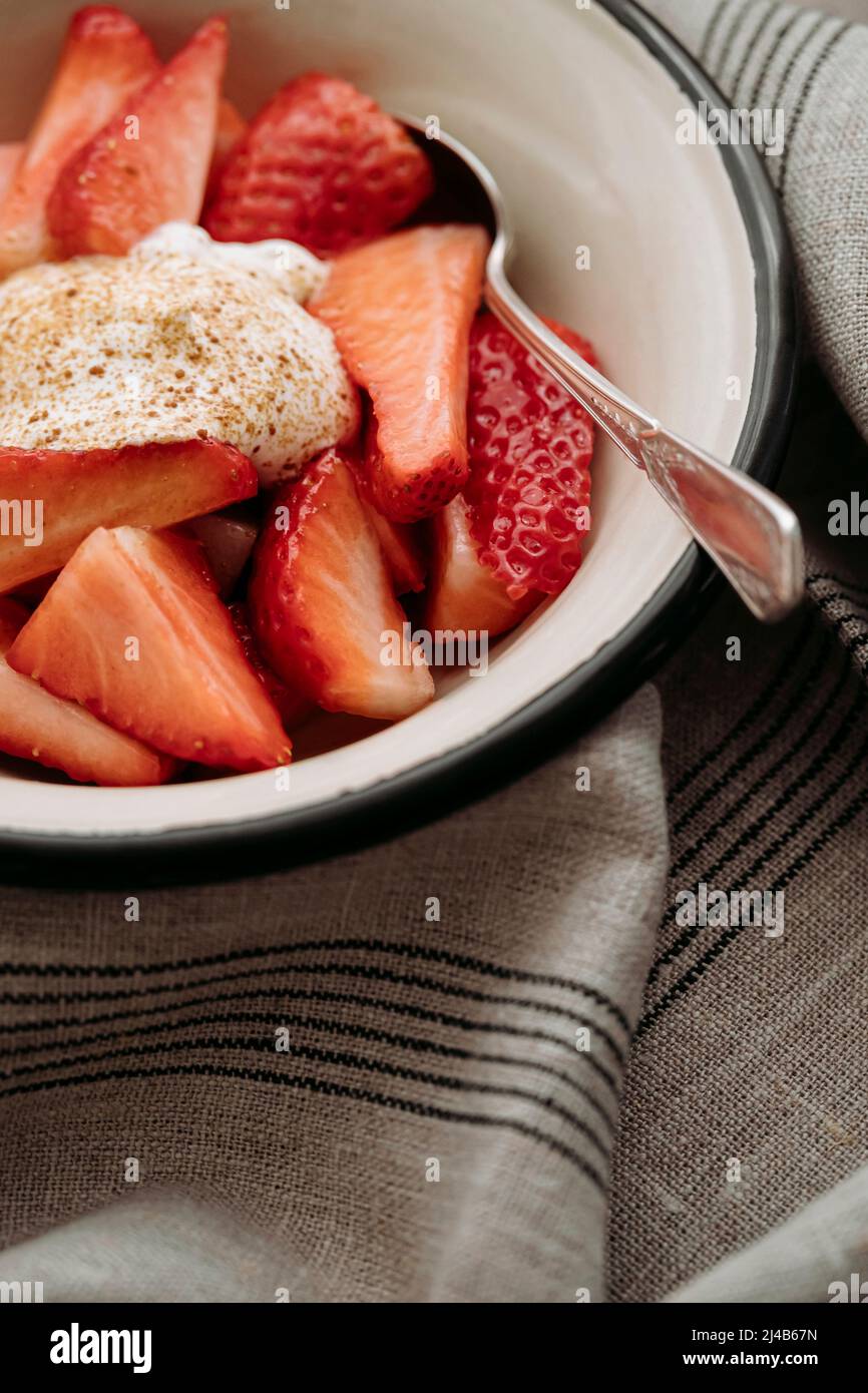 Metal bowl enamelled with slices of fresh strawberries and whipped cream and brown sugar Stock Photo