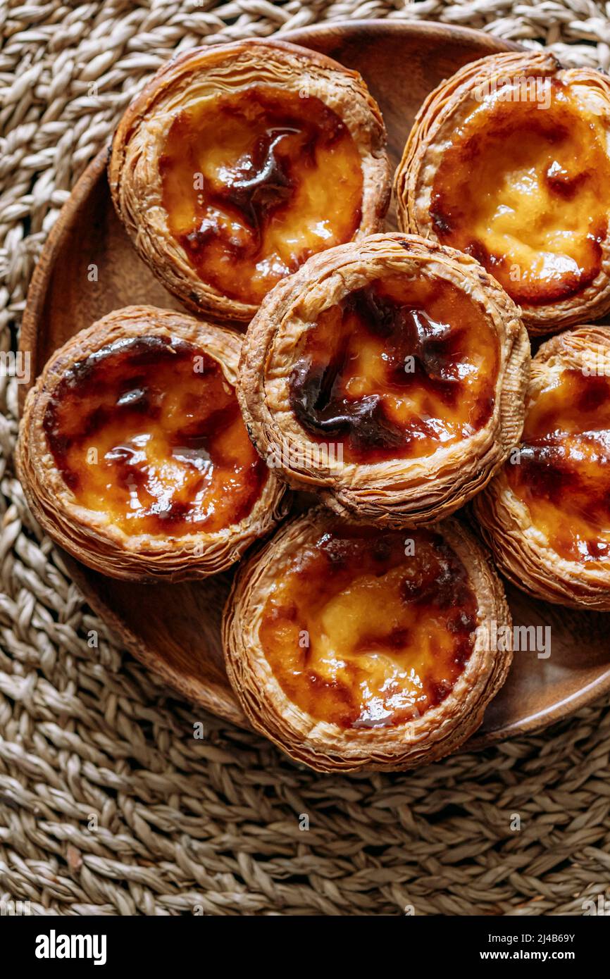 Top view of some Pasteis de nata (small traditional Portuguese cake) in a wooden plate, on a natural fiber trivet Stock Photo