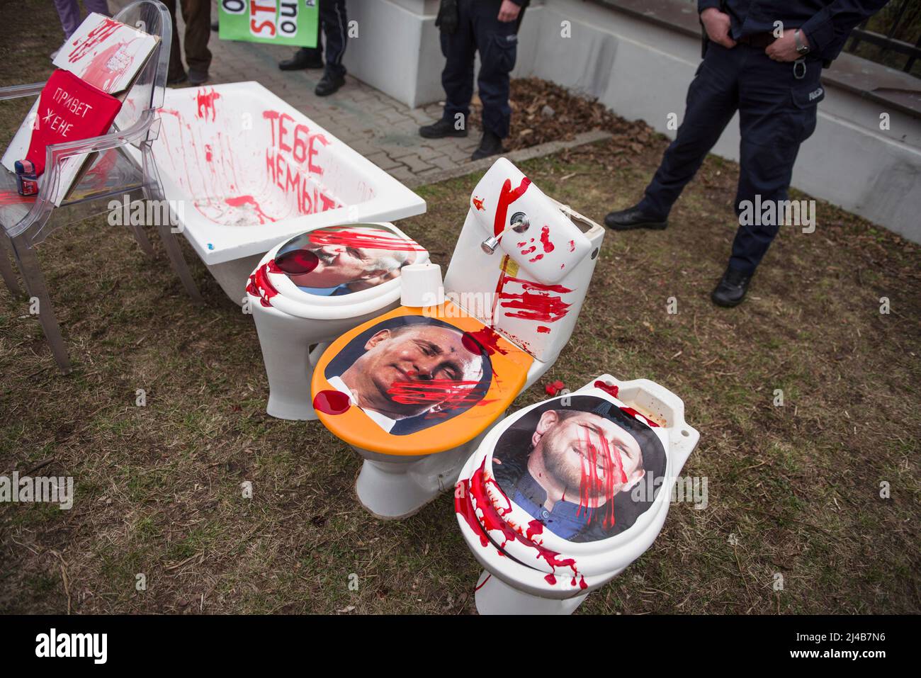 Police officers stand guard as toilet bowls with portraits of: from left to right, Belarusian President Alexander Lukashenko, Russian President Vladimir Putin and Chechnya's regional leader Ramzan Kadyrov are installed during a anti-Russian protest. An anti-Russian protest took place in Warsaw in front of the Russian embassy.Warsaw citizens and Ukrainians brought absolutely every junk that could be found in the basement to the embassy. All the rubbish was covered with red paint, which symbolizes the blood of murdered Ukrainian civilians. The action was aimed at publicizing the disgraceful beha Stock Photo