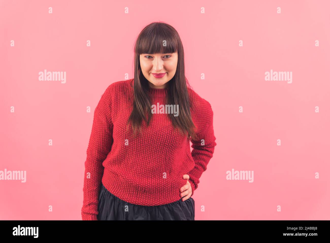 Medium shot pretty young Caucasian woman looking at the camera and smiling, keeping one hand on the waist pink background isolated copy space studio shot . High quality photo Stock Photo