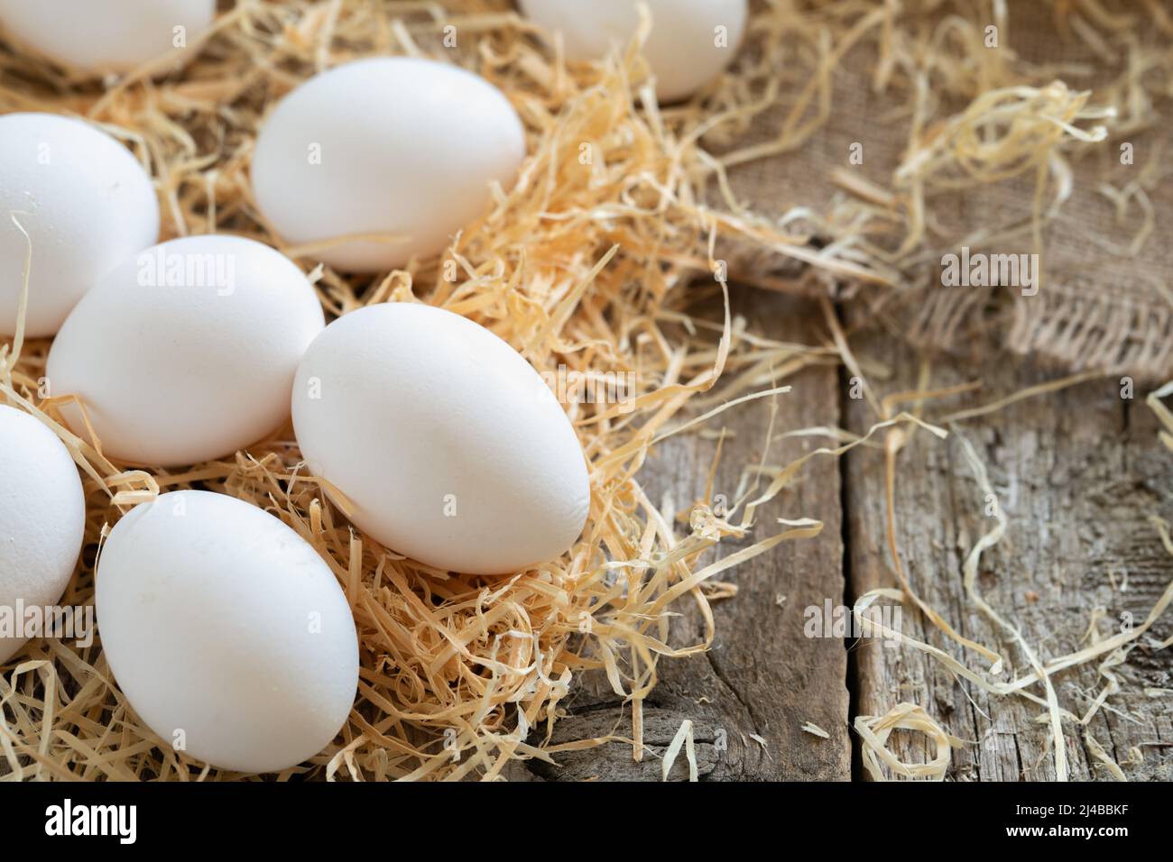 White chicken eggs on the straw or hay on burlap cloth and wooden ...