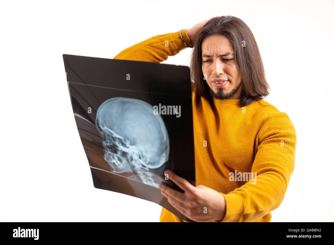 Young man holding and looking at head x-ray, touching head with his hand, sad emotions isolated studio shot copy space . High quality photo Stock Photo