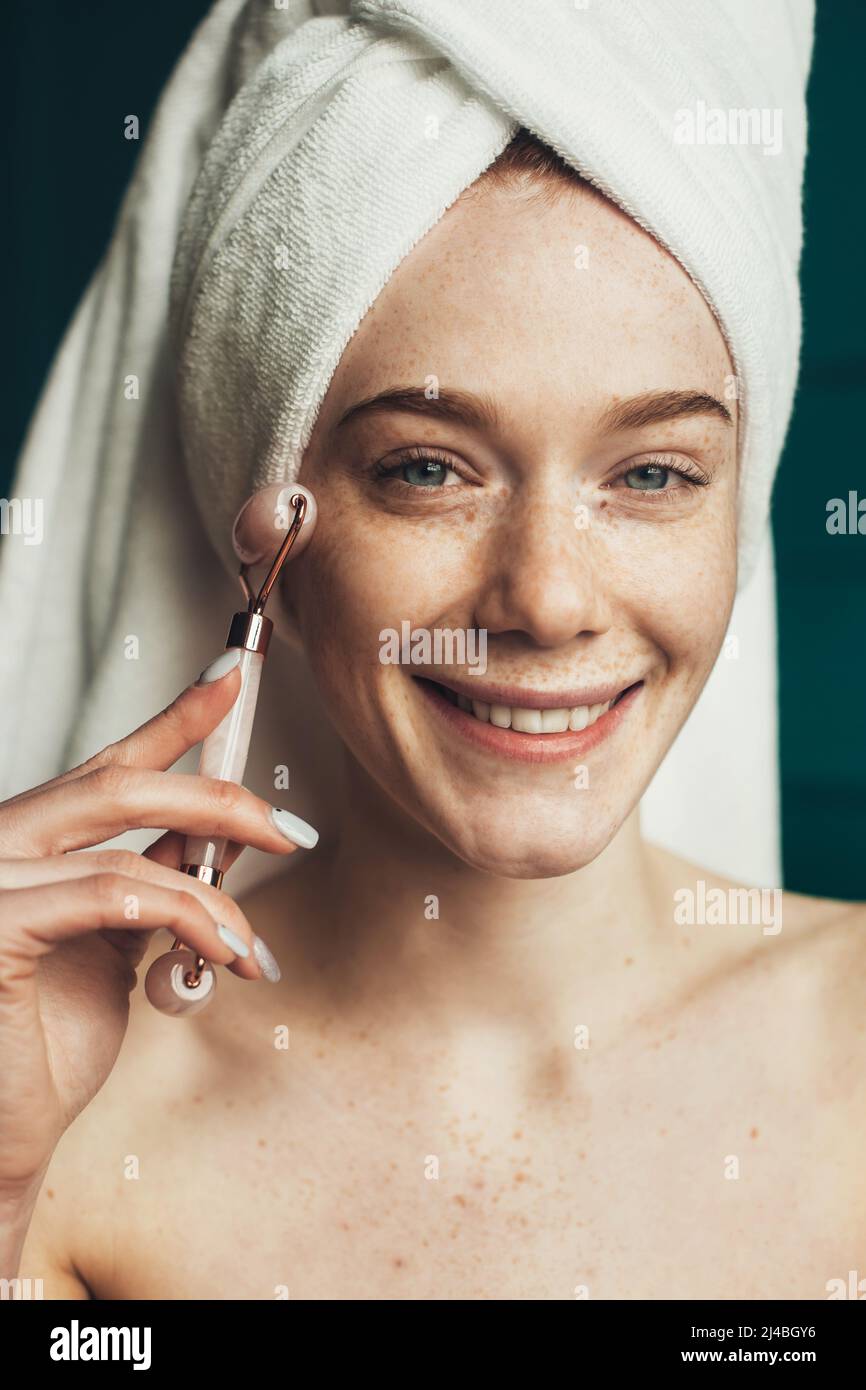 Freckled woman massaging face by jade roller massager after shower