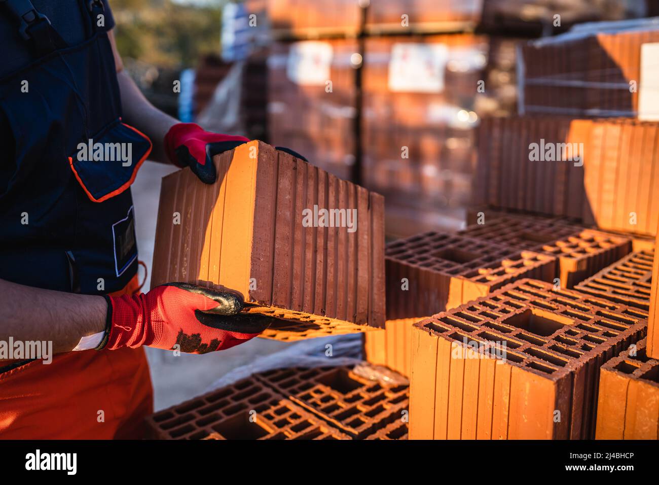 Close up on hands of unknown man construction worker taking hollow clay block ar warehouse or construction site in sunny summer day copy space Stock Photo