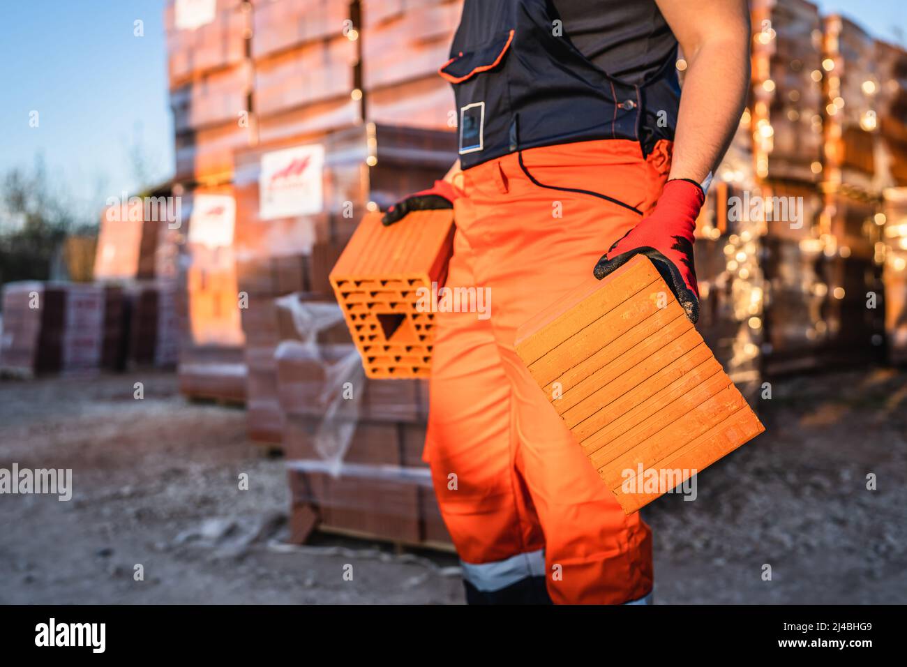 Close up on hands and midsection of unknown man construction worker taking orange hollow clay blocks ar warehouse or construction site in sunny summer Stock Photo