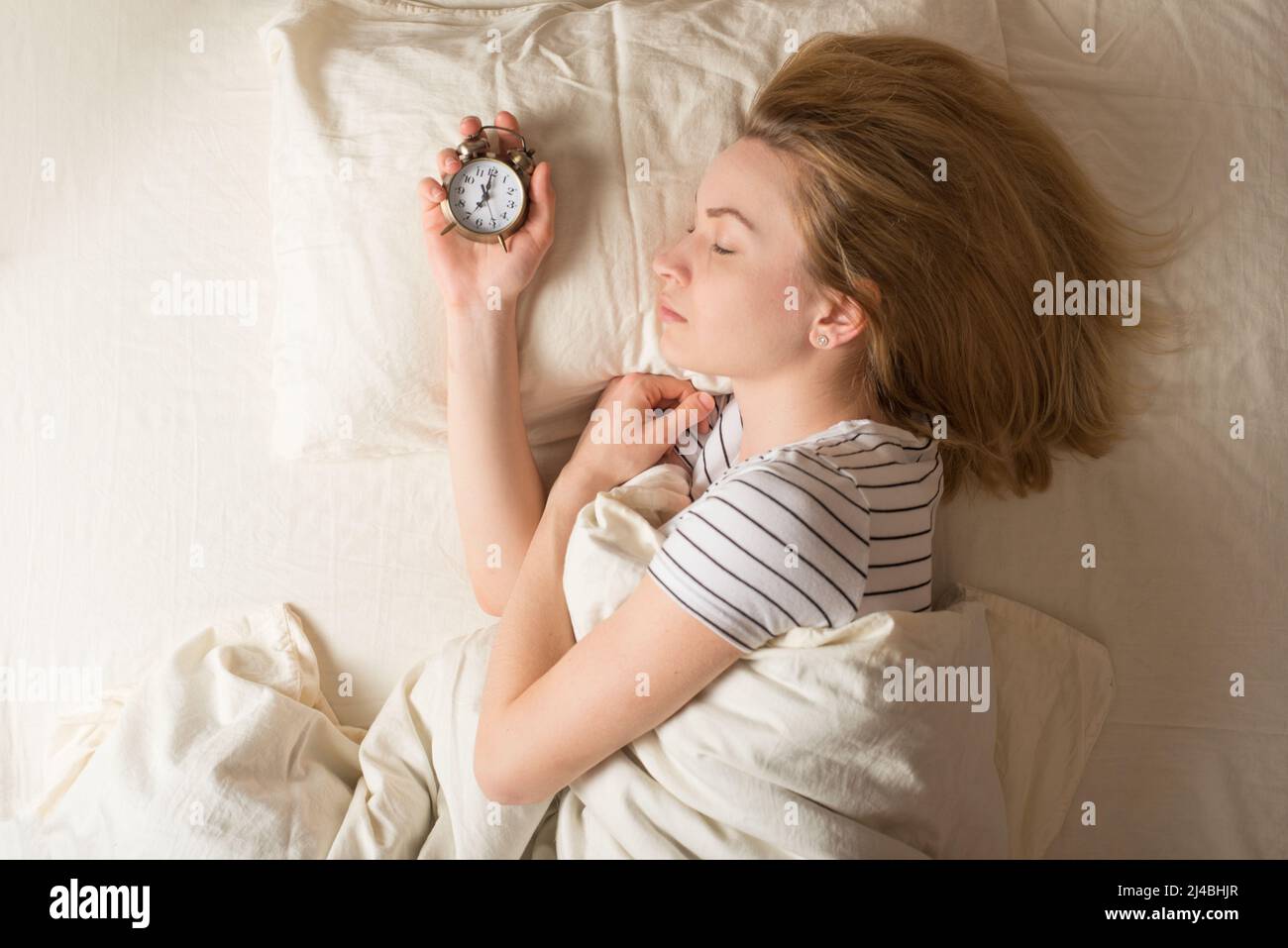 The girl wakes up the alarm clock in bed in the morning Stock Photo Alamy