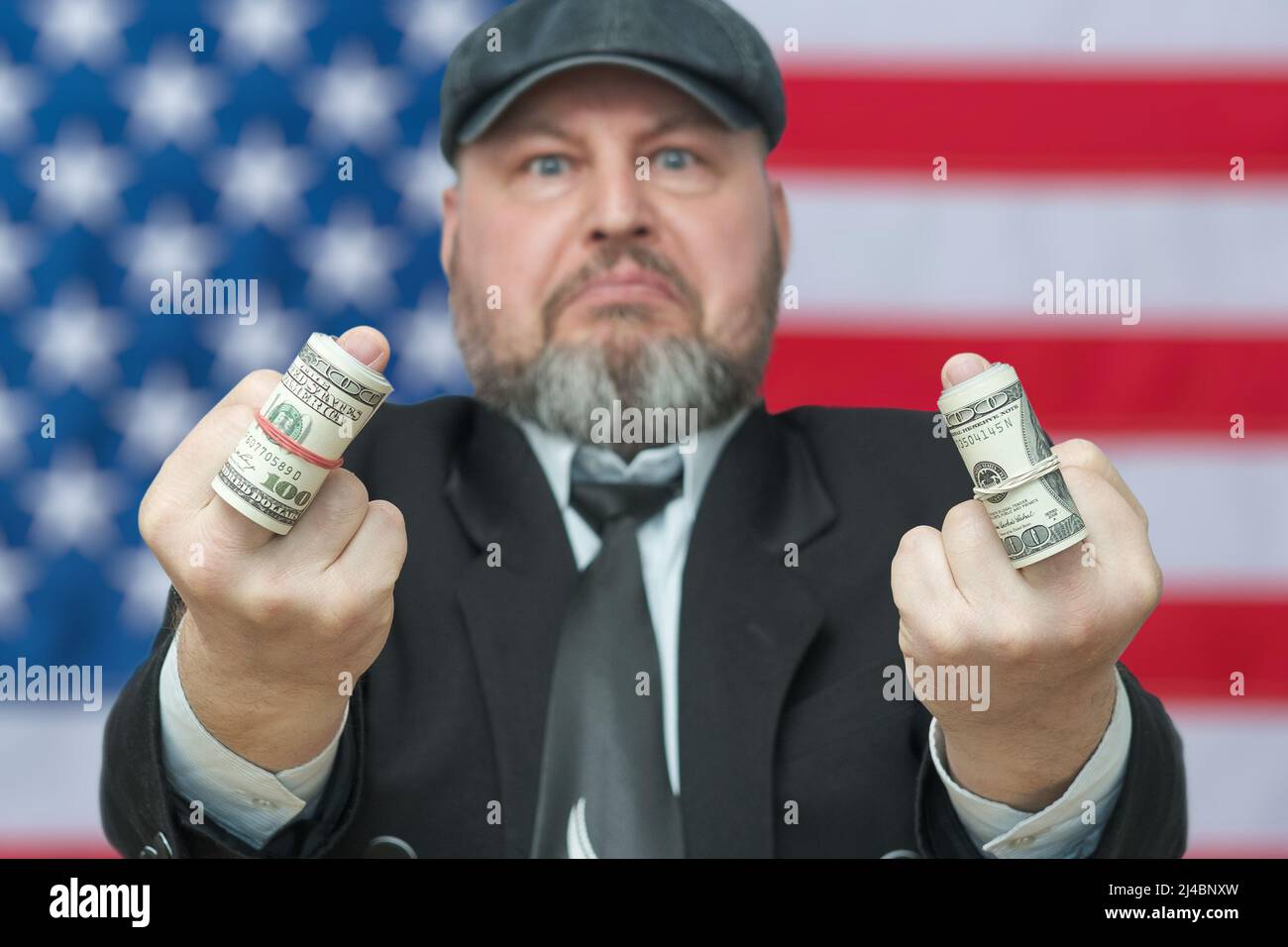 A man shows the middle finger on which dollars are rolled up into a tube. Gesture - you will not receive money. Against the background of the US flag. Stock Photo