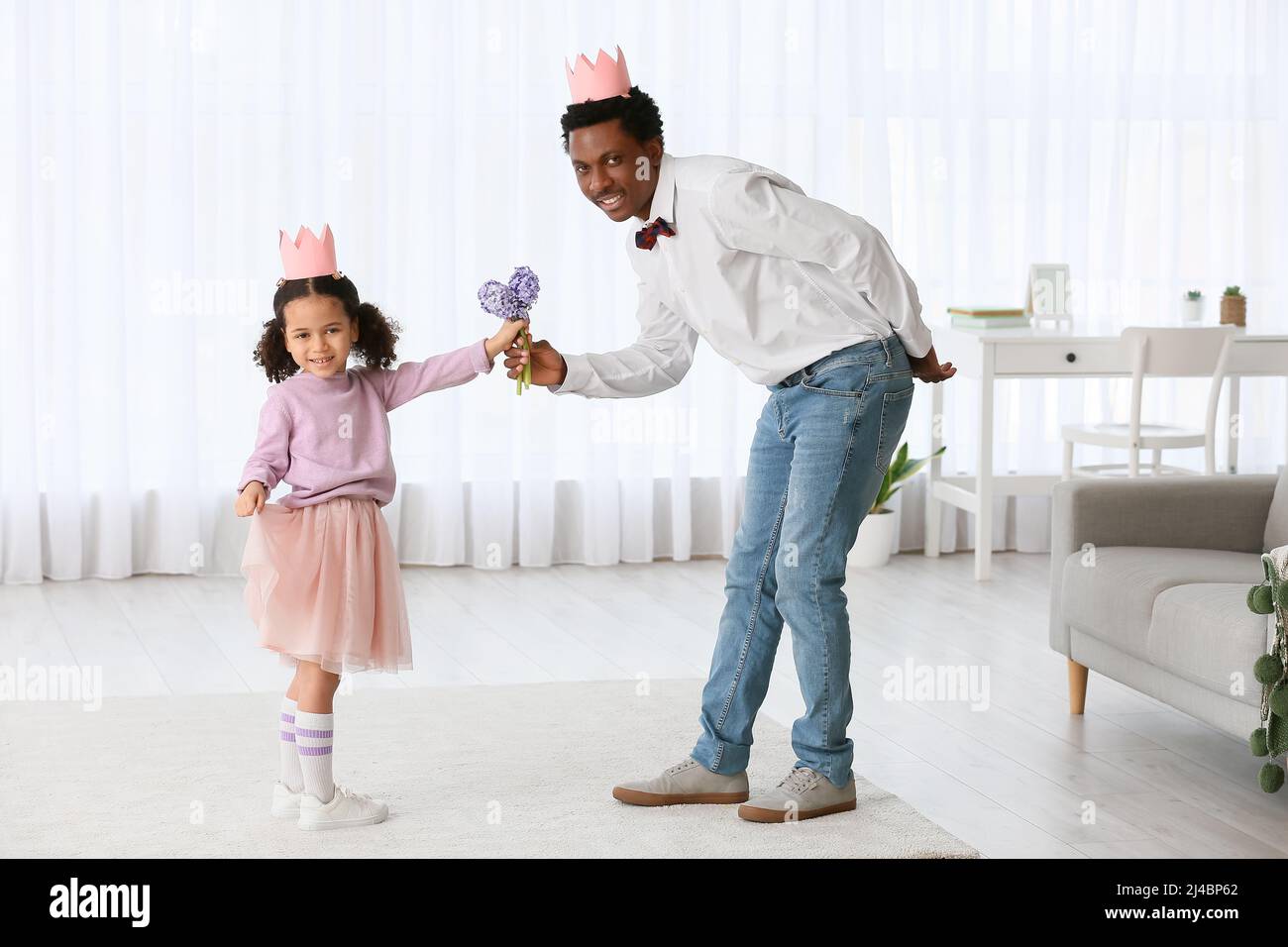 Happy African-American man giving flowers to his little daughter at home Stock Photo