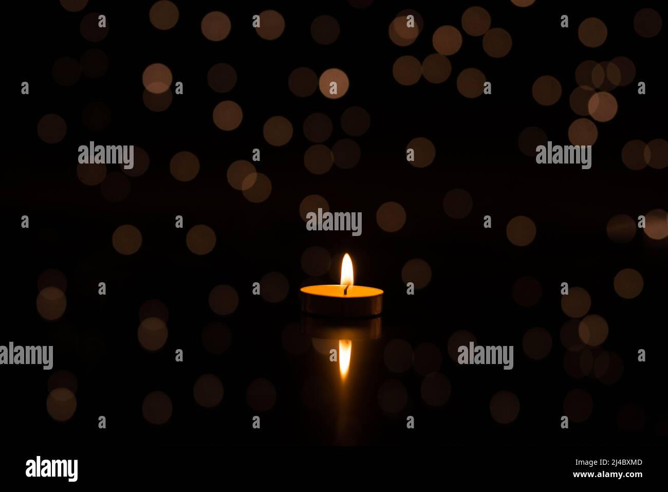 One candle in the dark with a reflection, in the background lights ...