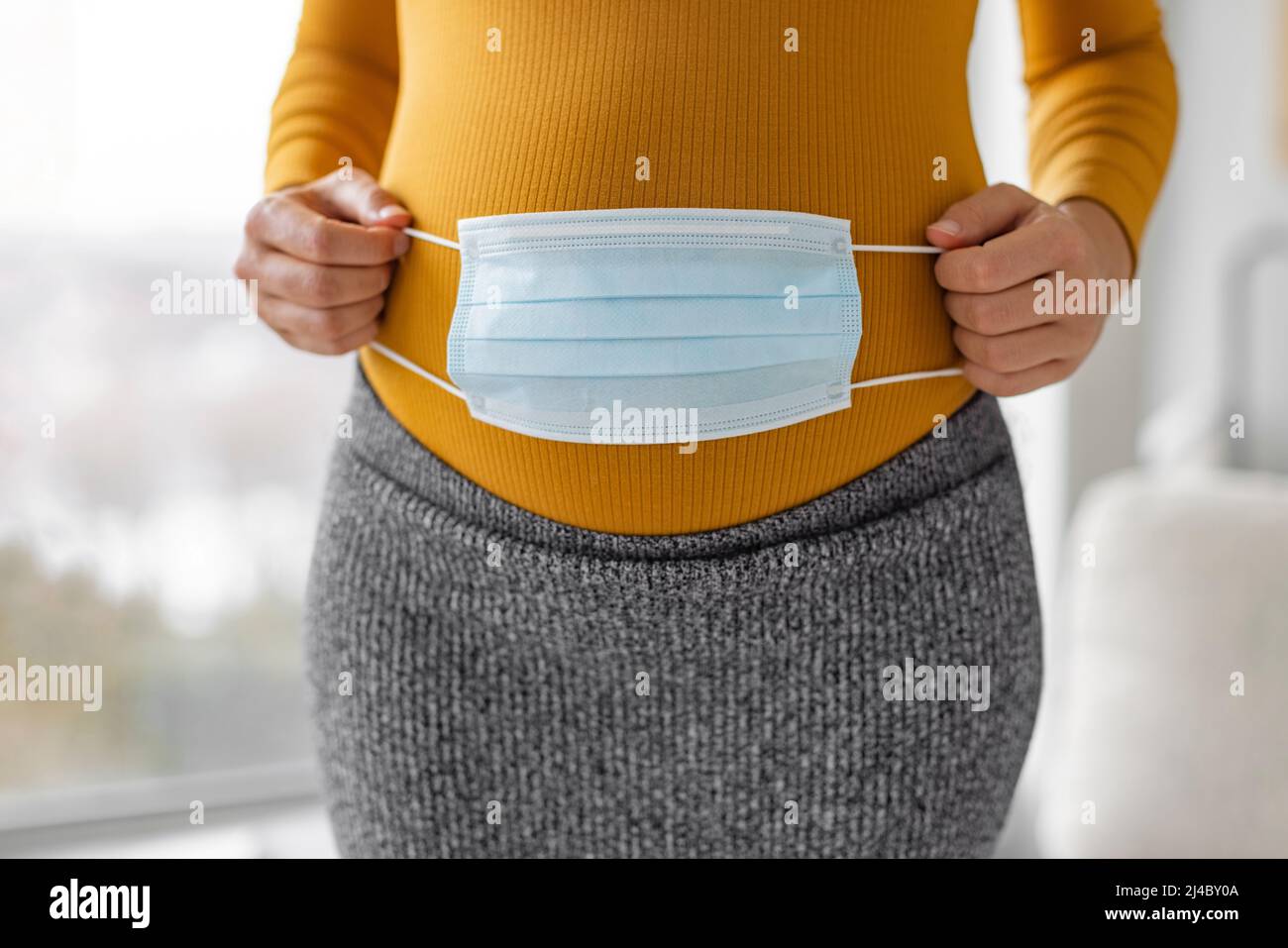Pregnancy during coronavirus pandemic. Pregnant woman covering belly with face mask for corona virus prevention concept. Pregnant women are at higher Stock Photo