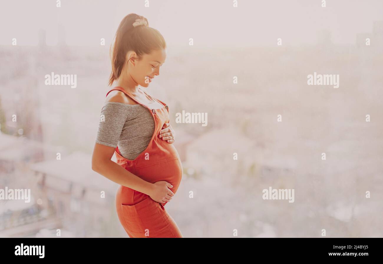 Asian pregnant woman happy touching her pregnancy bump for prenatal photoshoot wearing maternity clothes overalls. Beautiful young multiracial girl Stock Photo