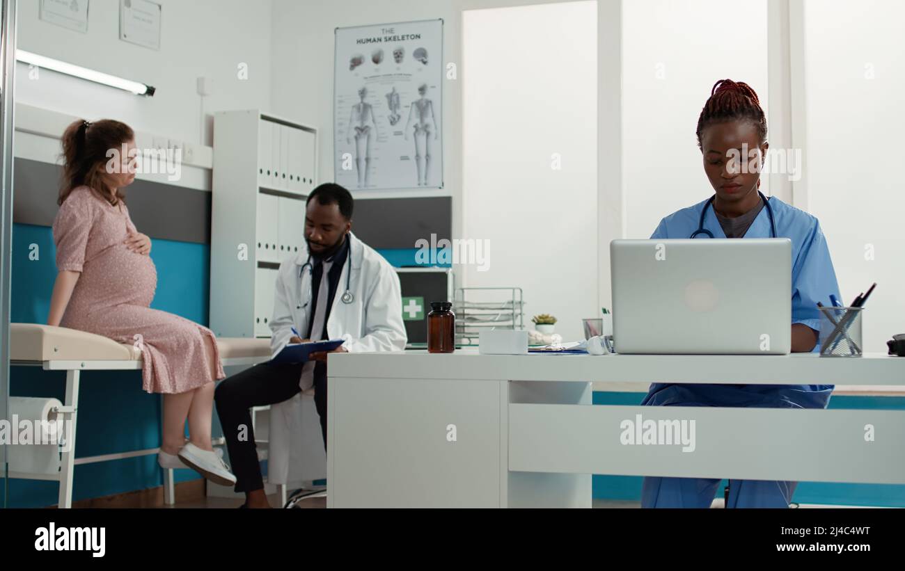 Medical assistant working on laptop in cabinet at appointment, helping ...