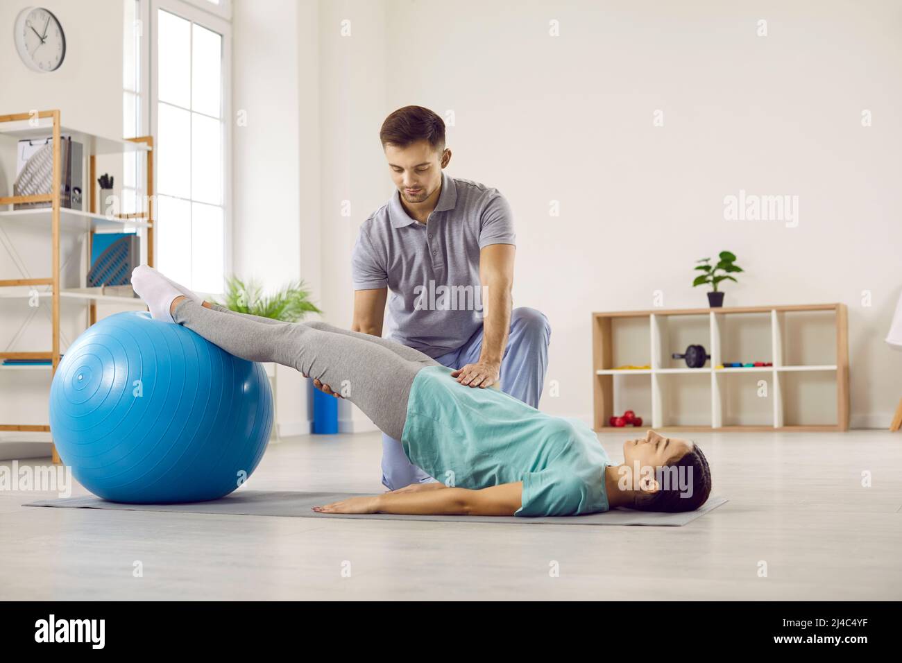 Physiotherapist helping his patient do physical rehabilitation exercises with fit ball Stock Photo