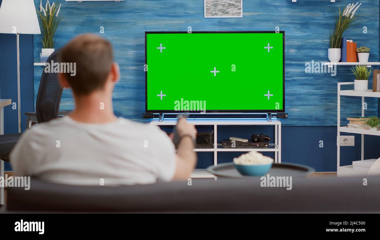 Man sitting on sofa looking at green screen on tv and switching