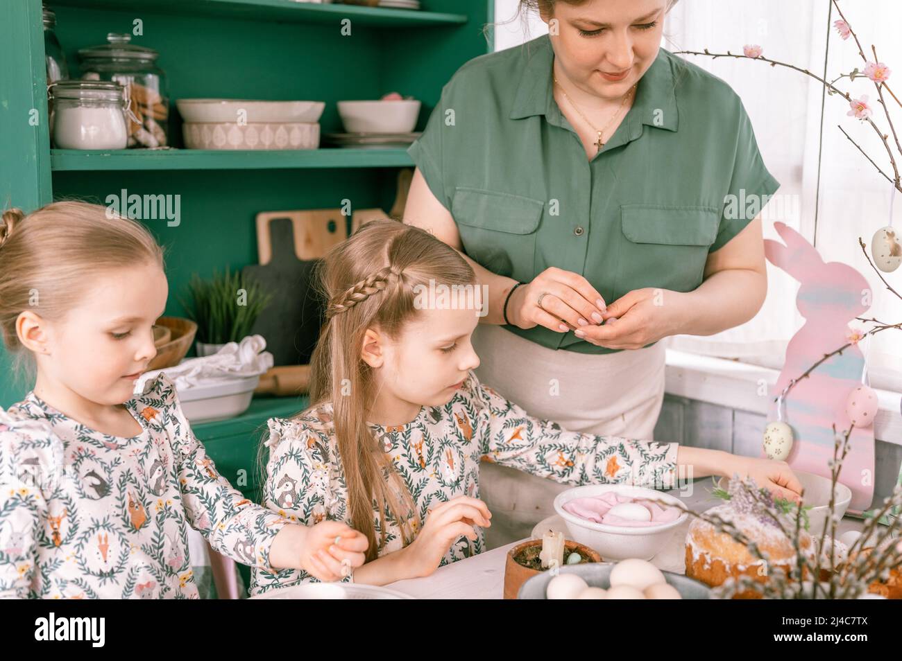 happy family mom together with little kids girls have fun springtime Easter holiday at home in kitchen setting and decorating table scape with Easter Stock Photo