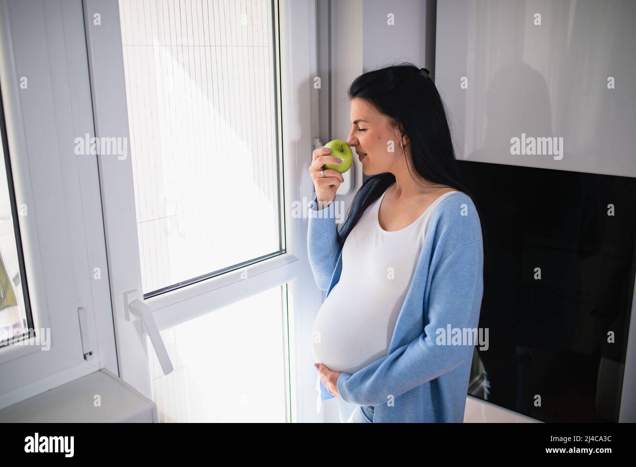 A young caucasian pregnant woman smells green apple while her eyes are