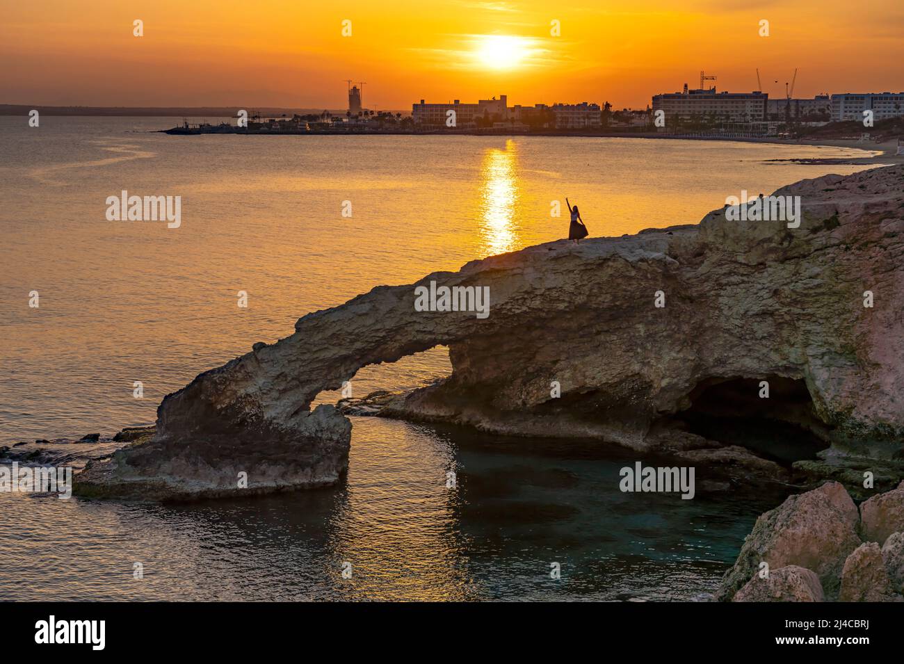 Junge Frau auf der natürlichen Felsenbrücke Love Bridge im Sonnenuntergang, Agia Napa, Zypern, Europa  | young woman posing on the natural  stone brid Stock Photo