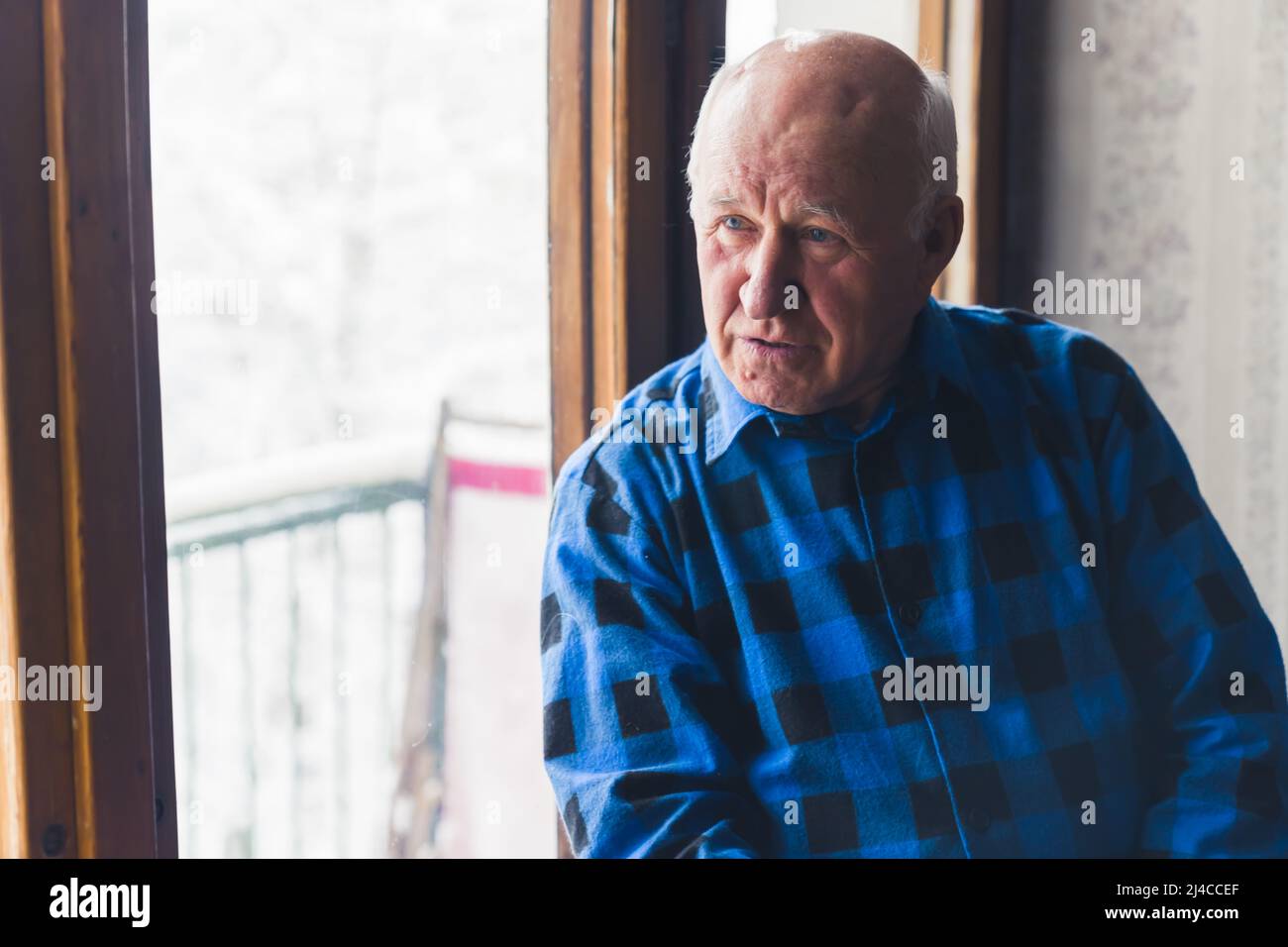 Caucasian balding senior grandfather sitting by the window with sad gaze. Indoor shot. High quality photo Stock Photo