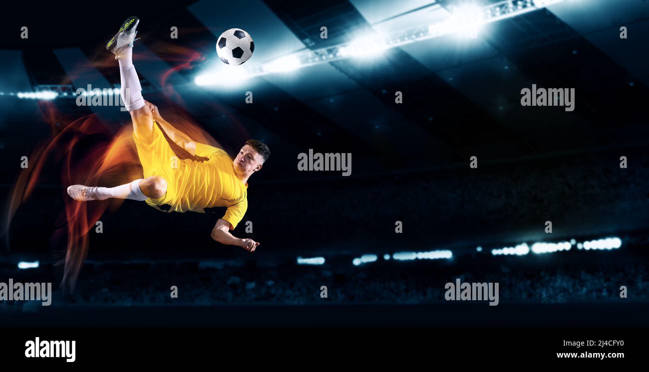 Active professional soccer, football player kick the ball in jump at dark night stadium with flashlights. Sport, competition, championship. Flyer Stock Photo