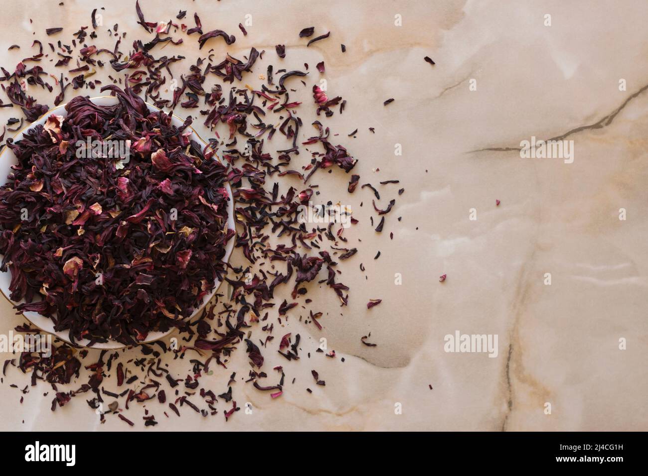 Dry hibiscus tea in a bowl. Dried hibiscus calyces, herbal tea made of crimson and deep magenta-colored sepals of the roselle flower, in the bowl on t Stock Photo