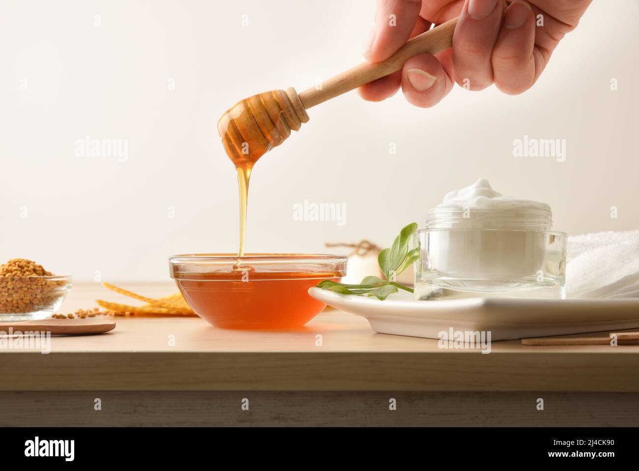 Cream with honey extracts and hand with stick showing honey and beeswax on a wooden table and isolated background. Horizontal composition. Front view. Stock Photo