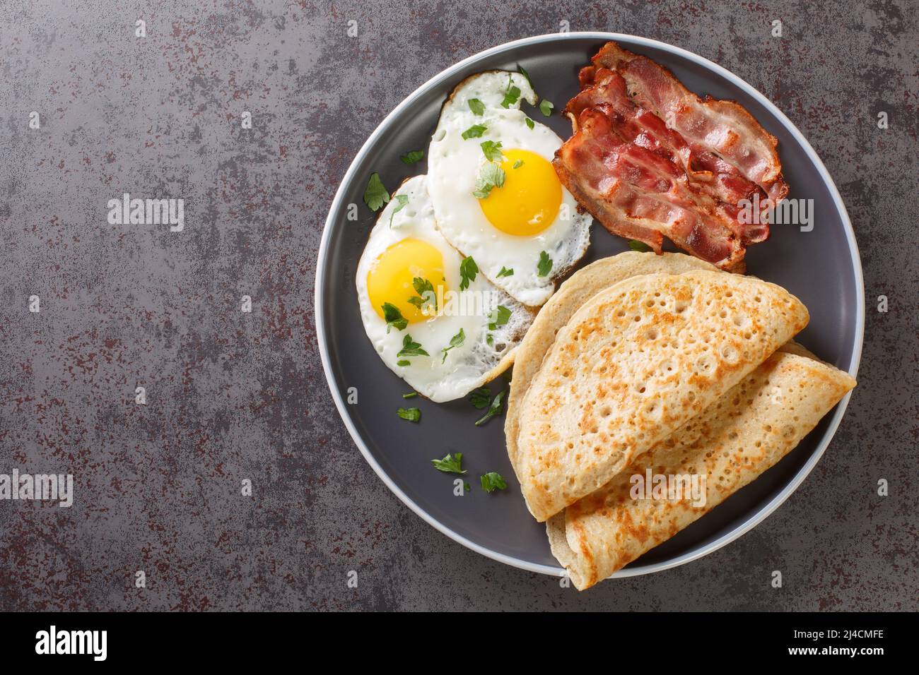 Savoury oat pancake perfect for breakfast with bacon and fried eggs close-up in a plate on the table. Horizontal top view from above Stock Photo