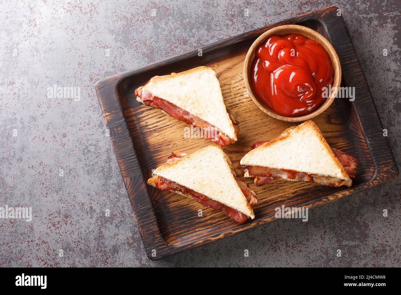 Sandwich with crispy bacon melted butter and ketchup close-up on a wooden tray on the table. horizontal top view from above Stock Photo