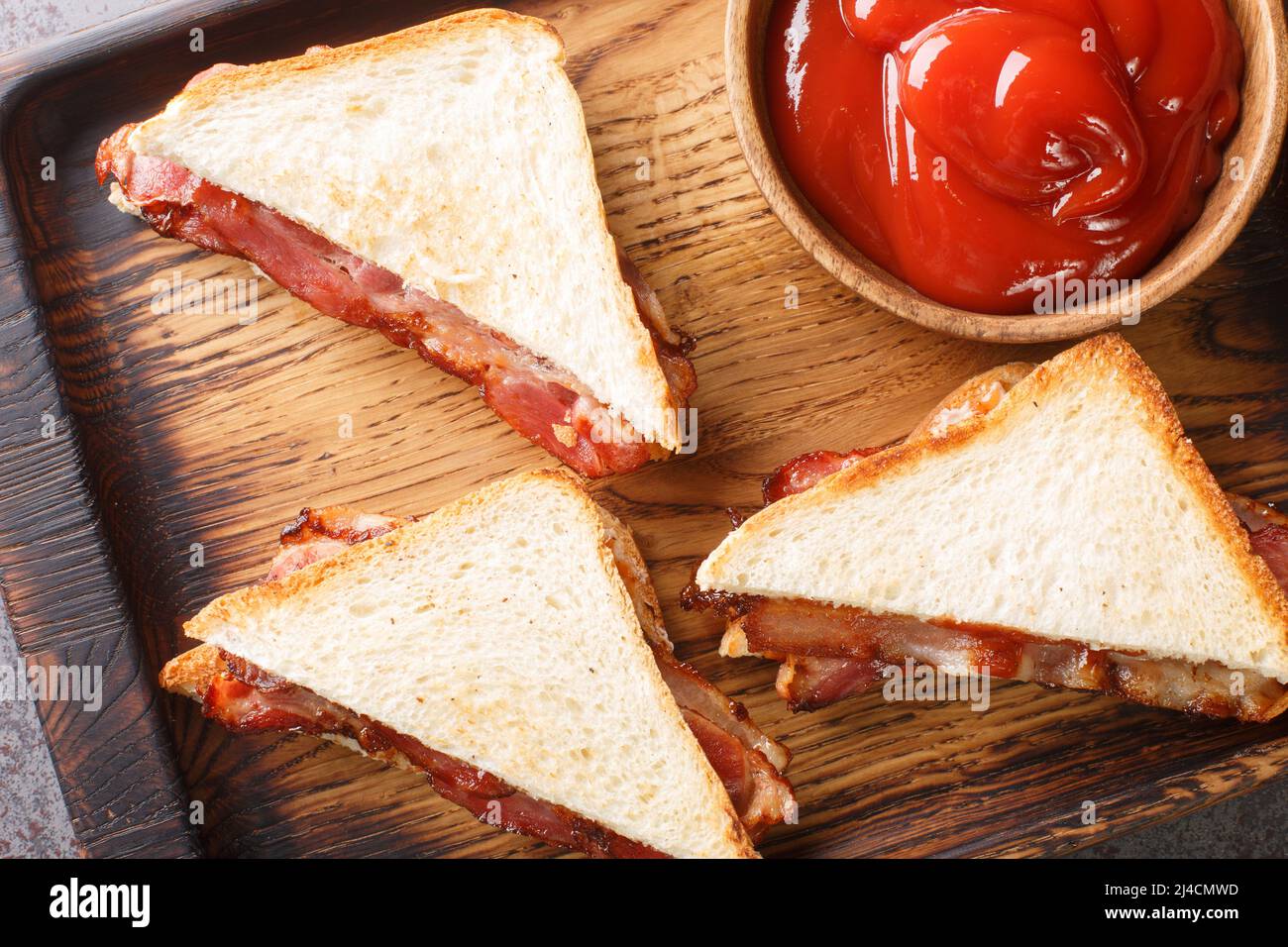 Bacon butty is a British sandwich consisting of crispy bacon, butter, and sauce closeup in the wooden tray on the table. Horizontal top view from abov Stock Photo