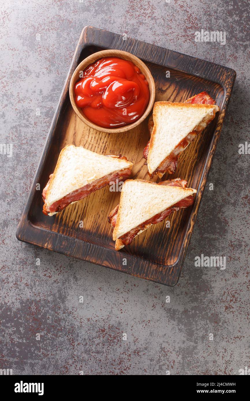 Bacon Butty sandwich with ketchup closeup in the wooden tray on the table. Vertical top view from above Stock Photo