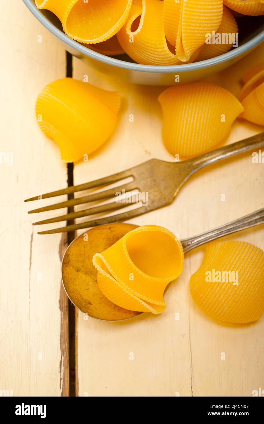 Raw Italian snail lumaconi pasta on a blue bowl over rustic table macro ...