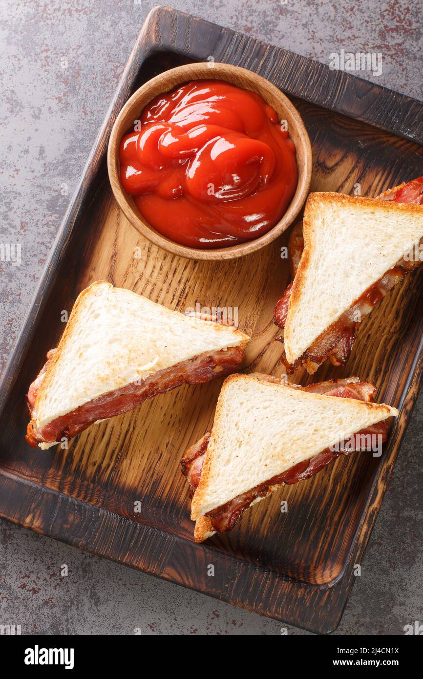 Bacon Butty  sandwich of fried bacon between bread that is optionally spread with butter, and may be seasoned with ketchup closeup in the wooden tray Stock Photo