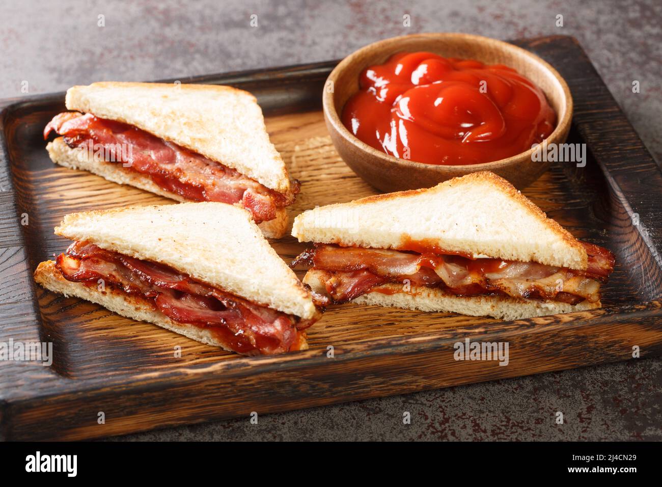 Sandwich with crispy bacon melted butter and ketchup close-up on a wooden tray on the table. horizontal Stock Photo