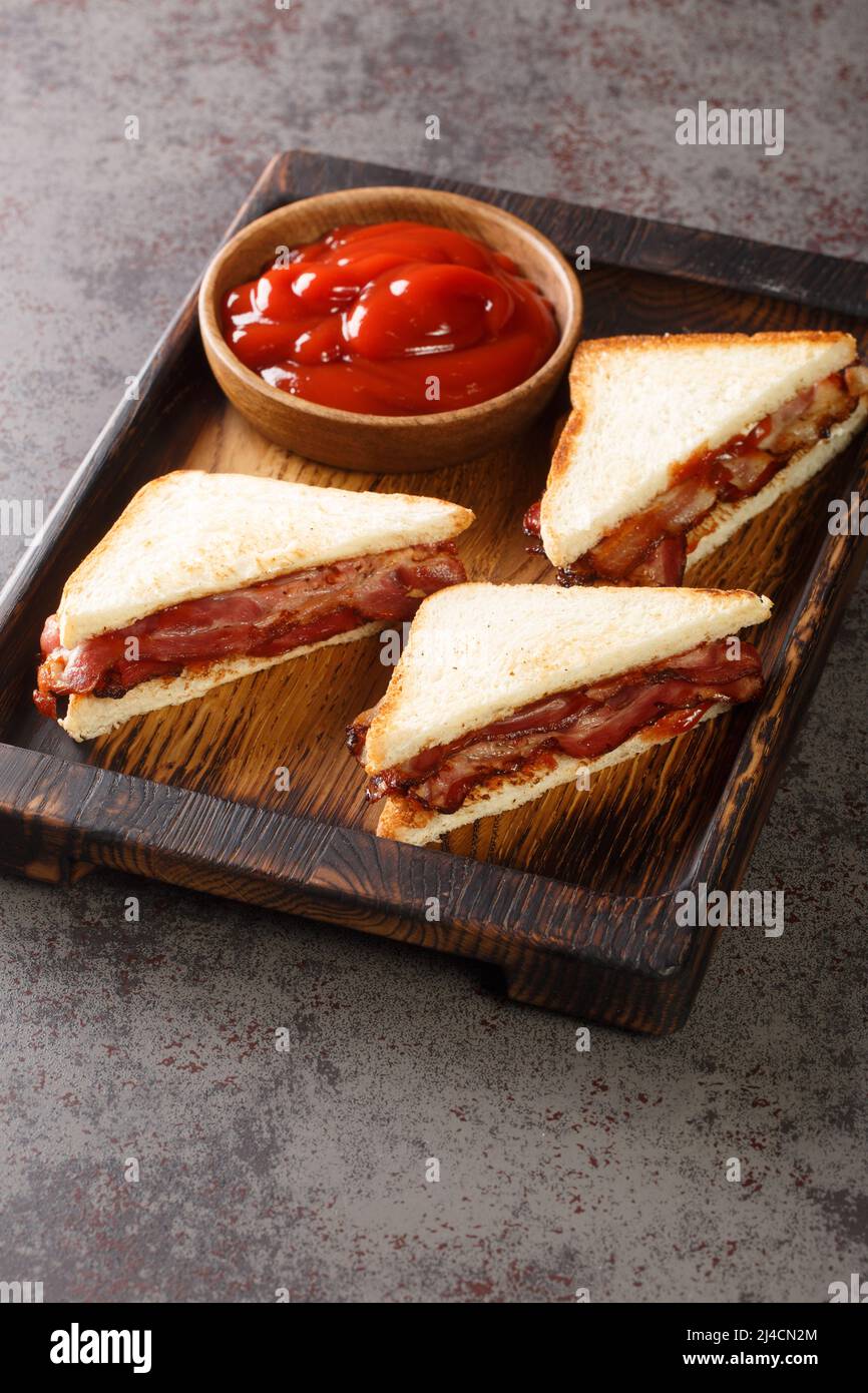 Bacon Butty  sandwich of fried bacon between bread that is optionally spread with butter, and may be seasoned with ketchup closeup in the wooden tray Stock Photo