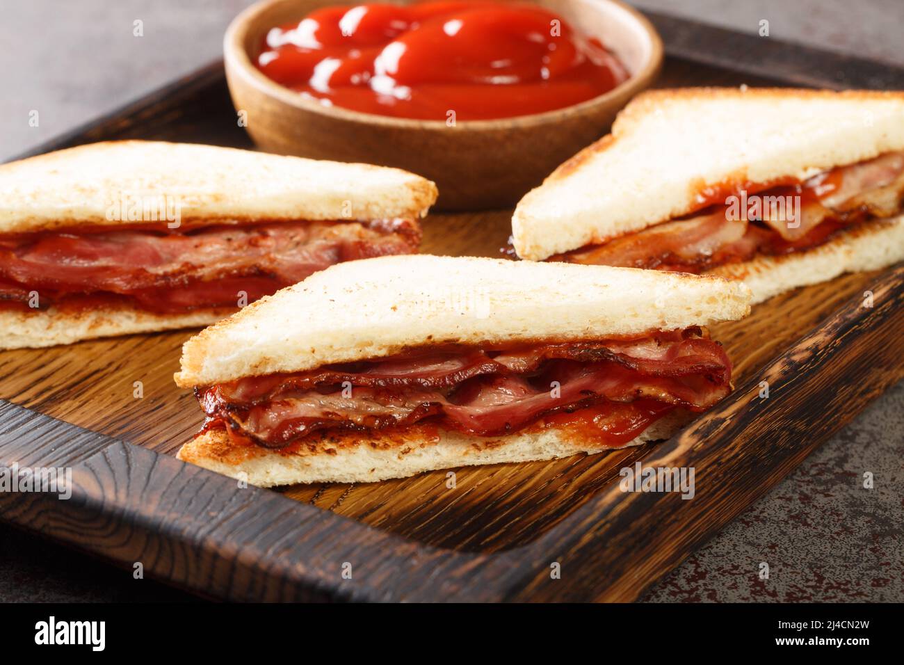Bacon Butty sandwich with ketchup closeup in the wooden tray on the table. horizontal Stock Photo