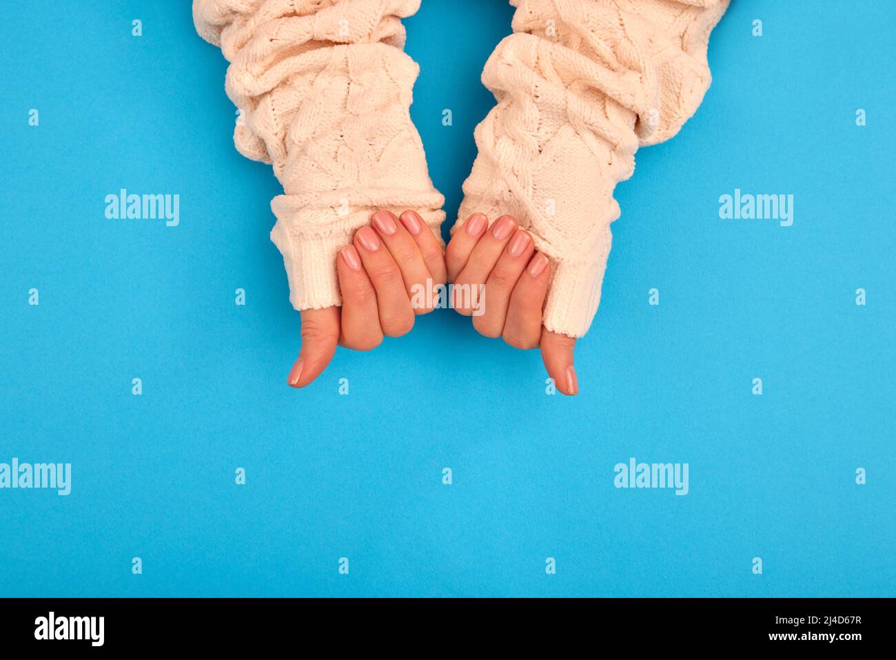 Neat manicure female hands sweater sleeves nude naturel on a blue background Stock Photo